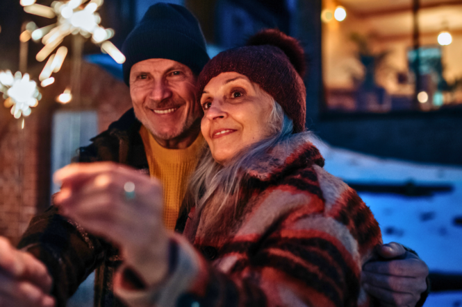 Happy senior couple celebrating new year with the sparklers, enjoying winter evening.