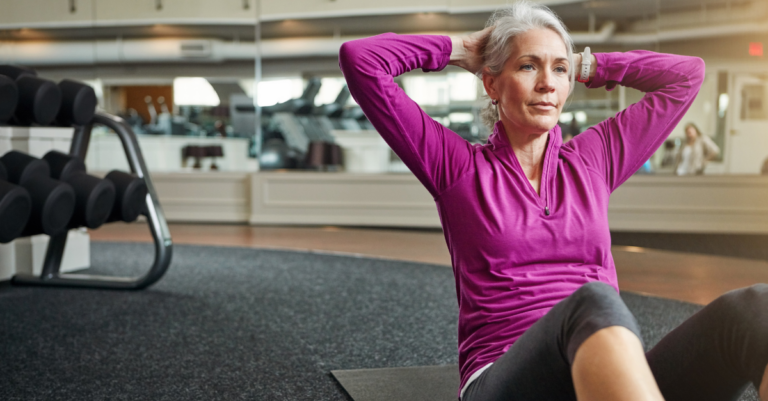 An older woman exercises at the gym doing curl-ups.
