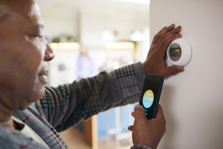 An older man uses an opp on his phone to control digital, arthritis-friendly thermostat.