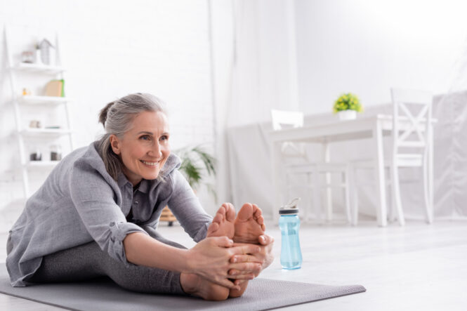 An older woman with joint pain takes time to stretch on her yoga mat.