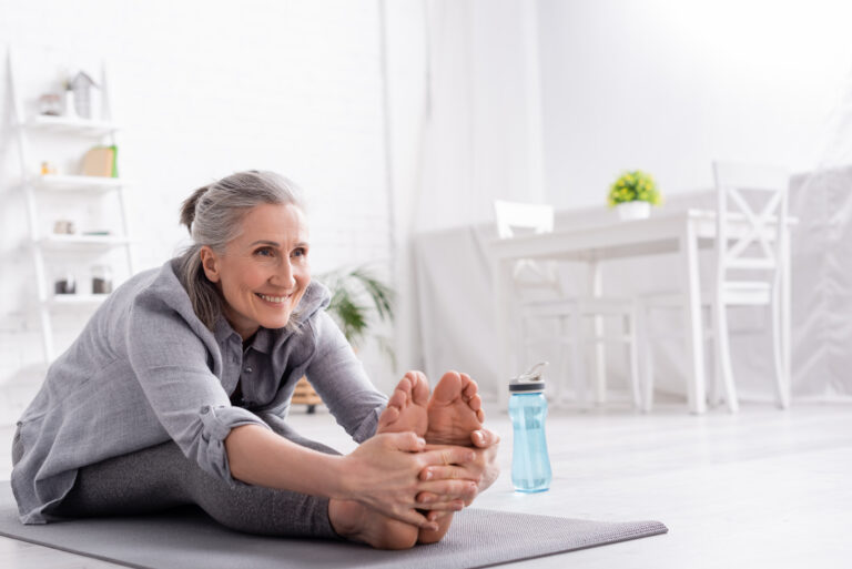 An older woman with joint pain takes time to stretch on her yoga mat.