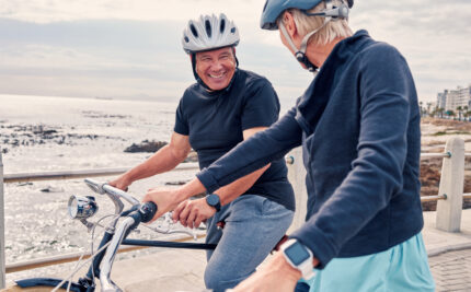 Older couple biking by the sea with helmets on